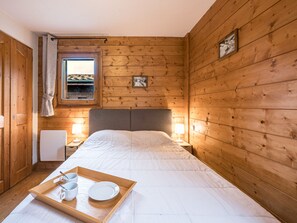 A wooden-paneled room with a bed, bedside lamps, a window, and a tray with cups and a plate. - Bright apartment near slopes (Les Menuires)