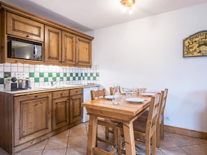 A kitchen with wooden cabinets, a microwave, a tiled backsplash, and a dining table with chairs. - Bright apartment near slopes (Les Menuires)