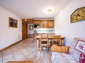 A kitchen with wooden cabinets, a tiled backsplash, and a dining table with chairs. - Bright apartment near slopes (Les Menuires)