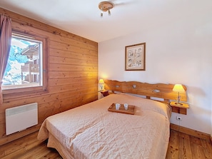 Ein Zimmer mit Holzwänden, einem Bett, zwei Nachttischlampen, einem gerahmten Bild und einem Fenster mit Vorhängen.