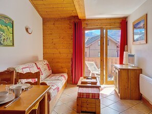 A cozy room with a wooden ceiling, a sofa, a dining table, and a television. - Spacious apartment, pets welcome - 4 guests (Les Menuires)