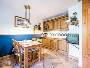 A kitchen with wooden cabinets, a tiled backsplash, a dining table with chairs, and a hanging light fixture. - Spacious 2-room apartment with balcony, near slopes, parking included (Les Menuires)