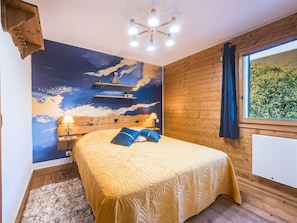 A bedroom with a bed, a nightstand, a wall mural, a window with curtains, and a ceiling light fixture. - Spacious 2-room apartment with balcony, near slopes, parking included (Les Menuires)