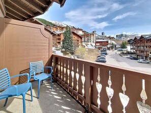 Un balcon avec des chaises bleues, une vue sur une montagne enneigée et un espace de stationnement avec des voitures.