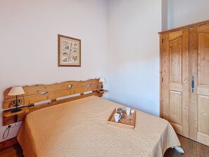 Une chambre à coucher avec un lit en bois, une table de chevet avec une lampe, un tableau encadré au mur et une armoire en bois.