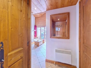 A wooden door leading into a room with a tiled floor, a radiator, and a view of a balcony with a red curtain. - Spacious apartment with balcony - 4 guests (Les Menuires)