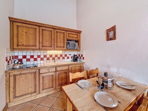 A kitchen with wooden cabinets, a tiled backsplash, and a dining table set with plates and glasses. - Spacious apartment with balcony - 4 guests (Les Menuires)
