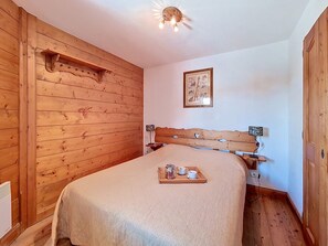 A wooden room with a bed, a bedside table, a wall-mounted light fixture, and a framed picture. - Spacious and bright apartment near slopes (Les Menuires)