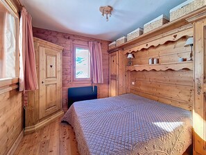 Ein Zimmer mit Holzboden, einem Bett, einem Vorhangfenster und einer Deckenleuchte.