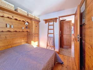 Ein Zimmer aus Holz mit einem Bett, einer Himmelsleiter und einer Tür zu einem anderen Raum.