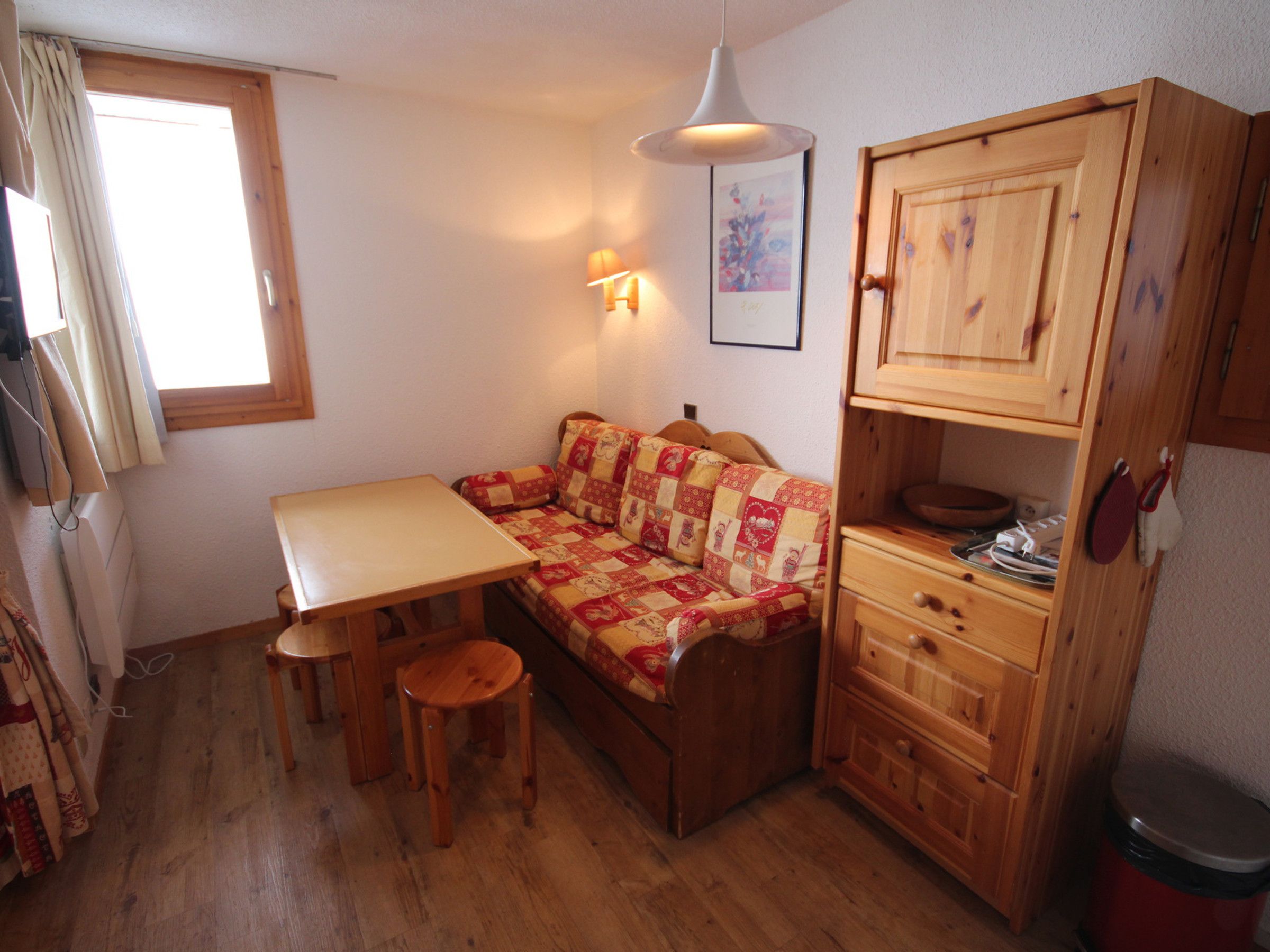 Een kleine kamer met een houten tafel, een bank en een kast met lades.