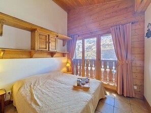 Ein Schlafzimmer mit einem Bett, einem Holzkopfstück, einem Fenster mit Vorhängen und einem Balkon mit Geländer.