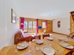 Un coin repas avec une table en bois dressée pour quatre personnes, un canapé et un téléviseur en arrière-plan.
