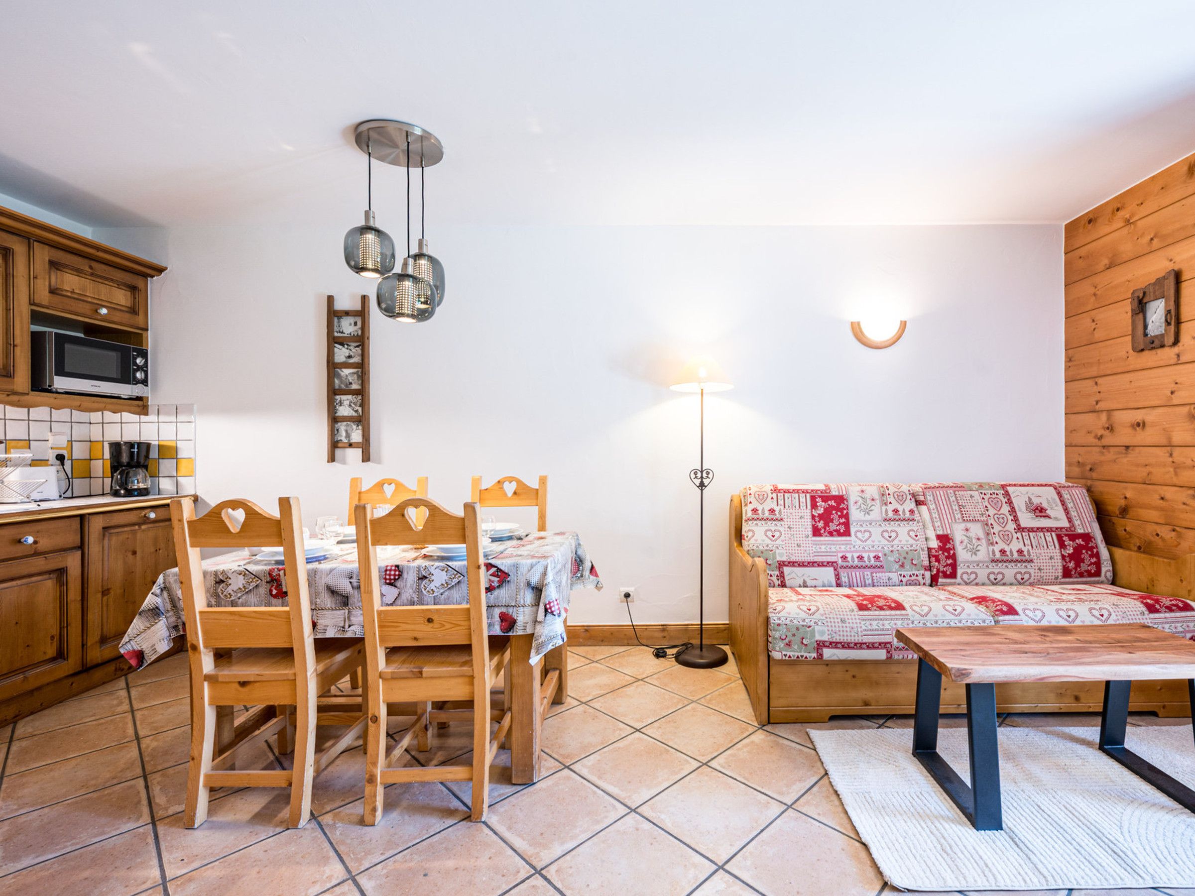 Un espace de vie chaleureux avec un canapé en bois, une table à manger avec des chaises, un coin cuisine équipé d’un four à micro-ondes et un luminaire fixé au mur.