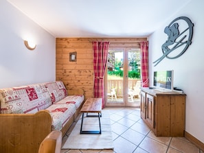 Une pièce chaleureuse avec un mur en bois, un canapé, un banc, un téléviseur et une vue sur l’extérieur.