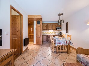 A kitchen with wooden cabinets, a dining table set for four, and a microwave. - Spacious apartment near the slopes - 4 guests (Les Menuires)