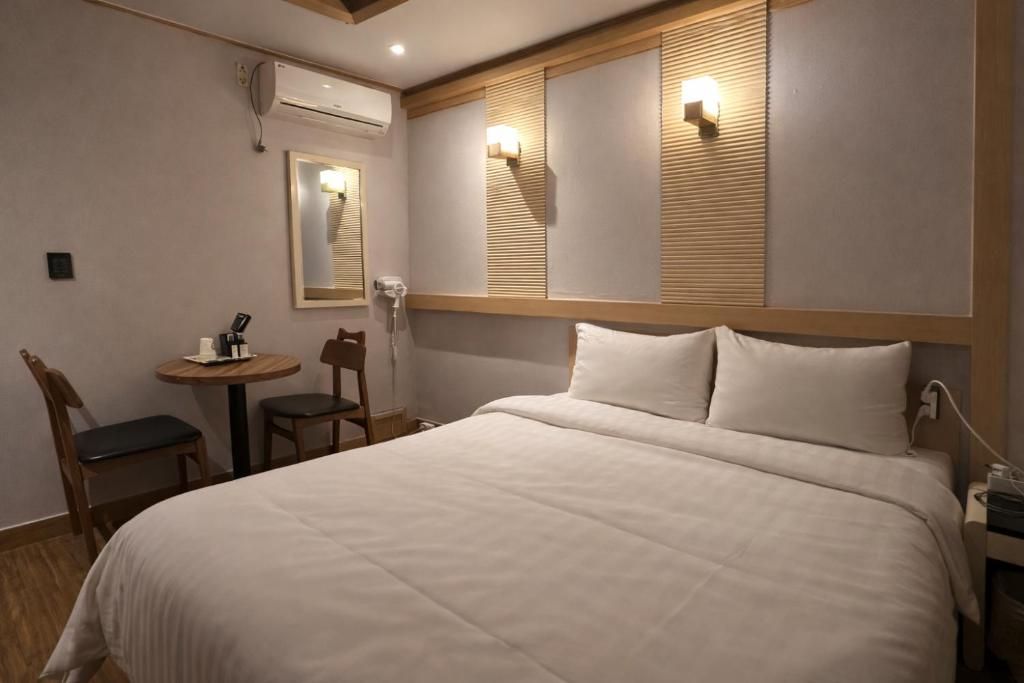 A hotel room with a large bed, a small round table, two chairs, a mirror, and a wall-mounted air conditioner.