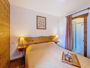 A bedroom with a wooden headboard, two bedside lamps, a framed picture on the wall, and a tray with cups and a teapot on the bed. - Spacious apartment with terrace - 6 guests (Les Menuires)