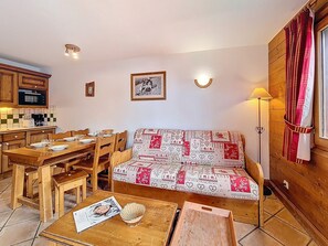 Un salon confortable avec un canapé, une table à manger et des chaises, une cuisine dotée de meubles en bois et un luminaire fixé au mur.