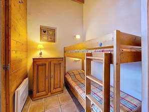 A bunk bed with a plaid bedspread, a wooden wardrobe, a wall-mounted lamp, and a decorative wall piece. - Superb apartment near the slopes (Les Menuires)
