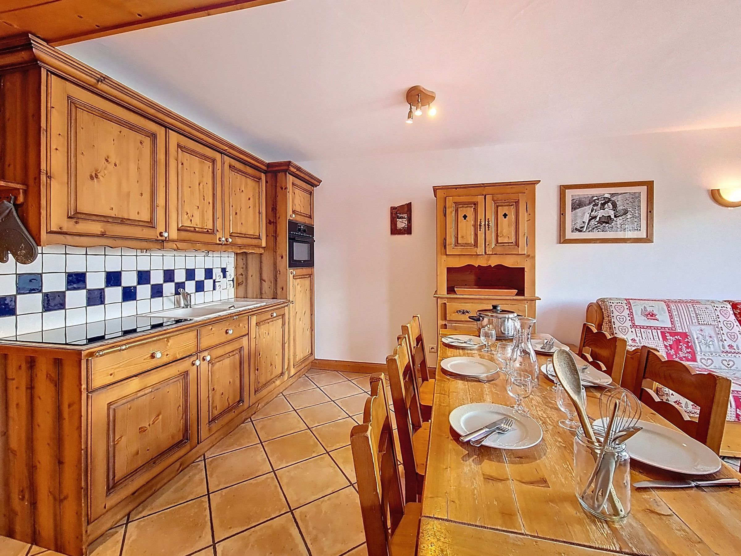 Una cucina con mobili in legno, zoccolo paraschizzi in piastrelle e un'area pranzo con tavolo apparecchiato per due.