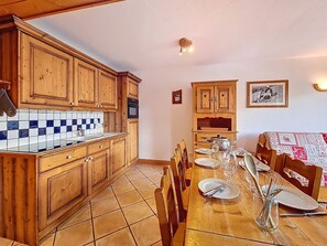 Una cocina con armarios de madera, salpicadero de azulejos y una zona de comedor con una mesa dispuesta para dos personas.