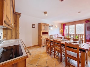 A dining area with a wooden table set for four, a kitchen with wooden cabinets, and a window with curtains. - Superb apartment near the slopes (Les Menuires)