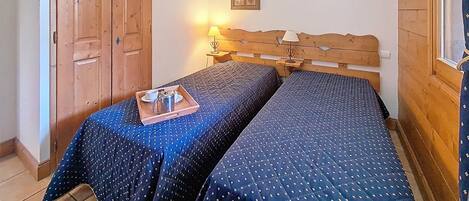 Una habitación con dos camas, un armario de madera y una lámpara de pared.