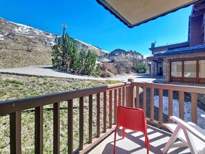 Un balcon avec une chaise rouge, une vue sur une montagne et un télésiège en arrière-plan.