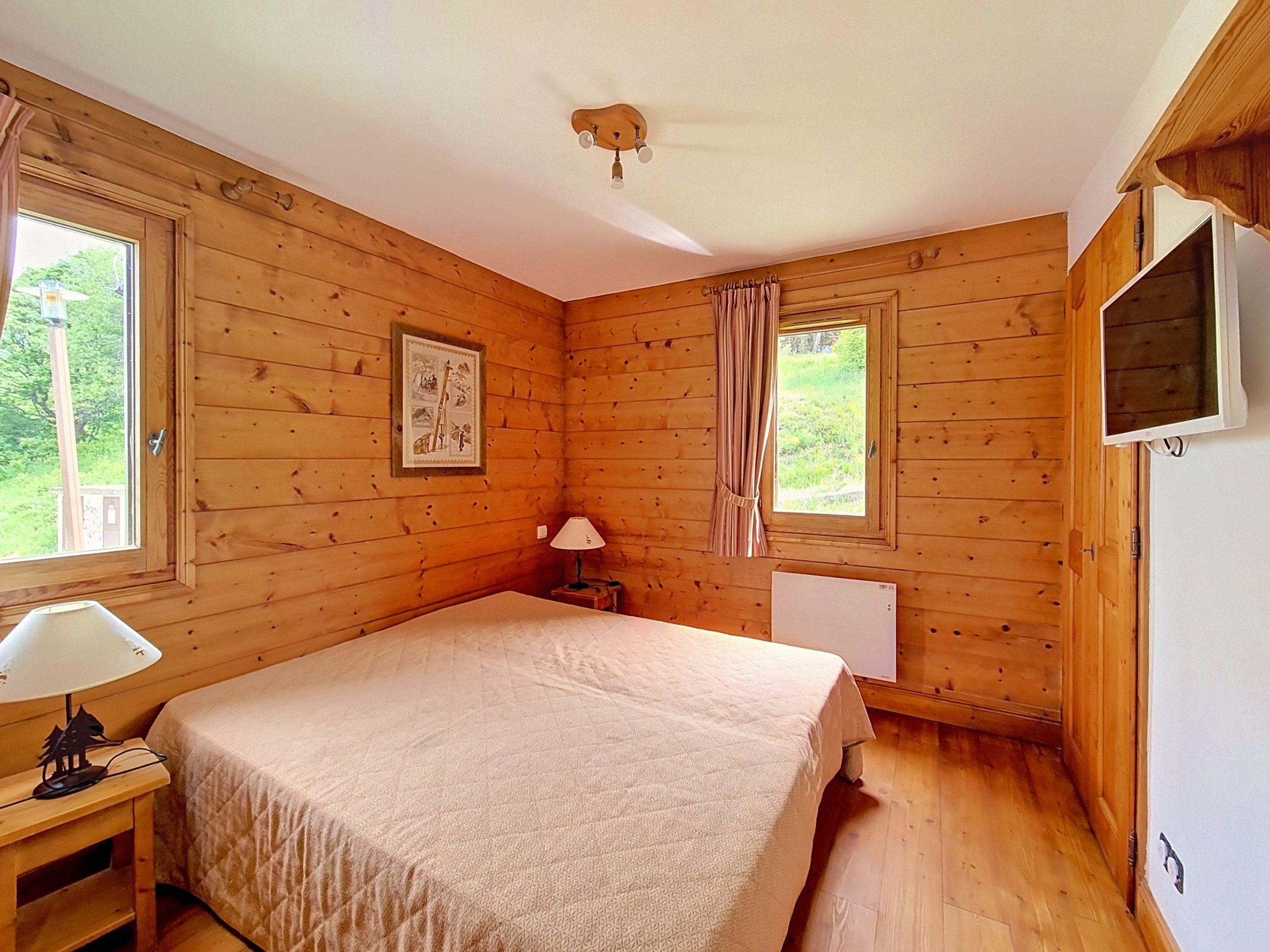 Una stanza in legno con un letto, una finestra, una lampada e una televisione.