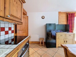 Eine Küche mit Holzausstattung, einem schwarzen Kühlschrank, einer gefliesten Spritzschutzwand und einem kleinen Hocker.