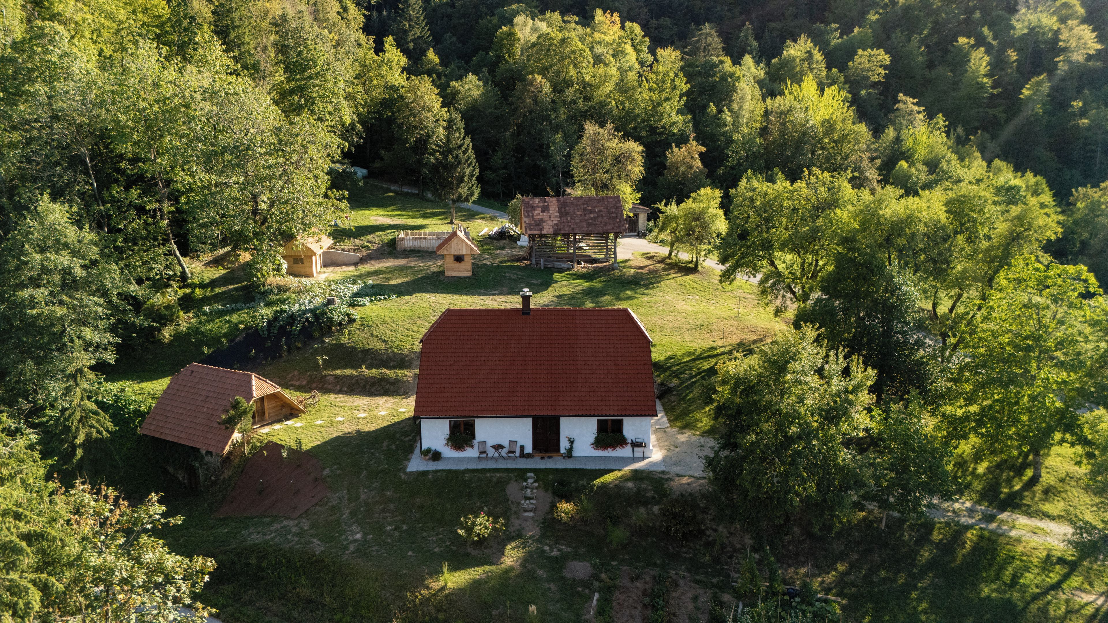 Una casa rural con techo rojo, rodeada de árboles y un pequeño jardín.