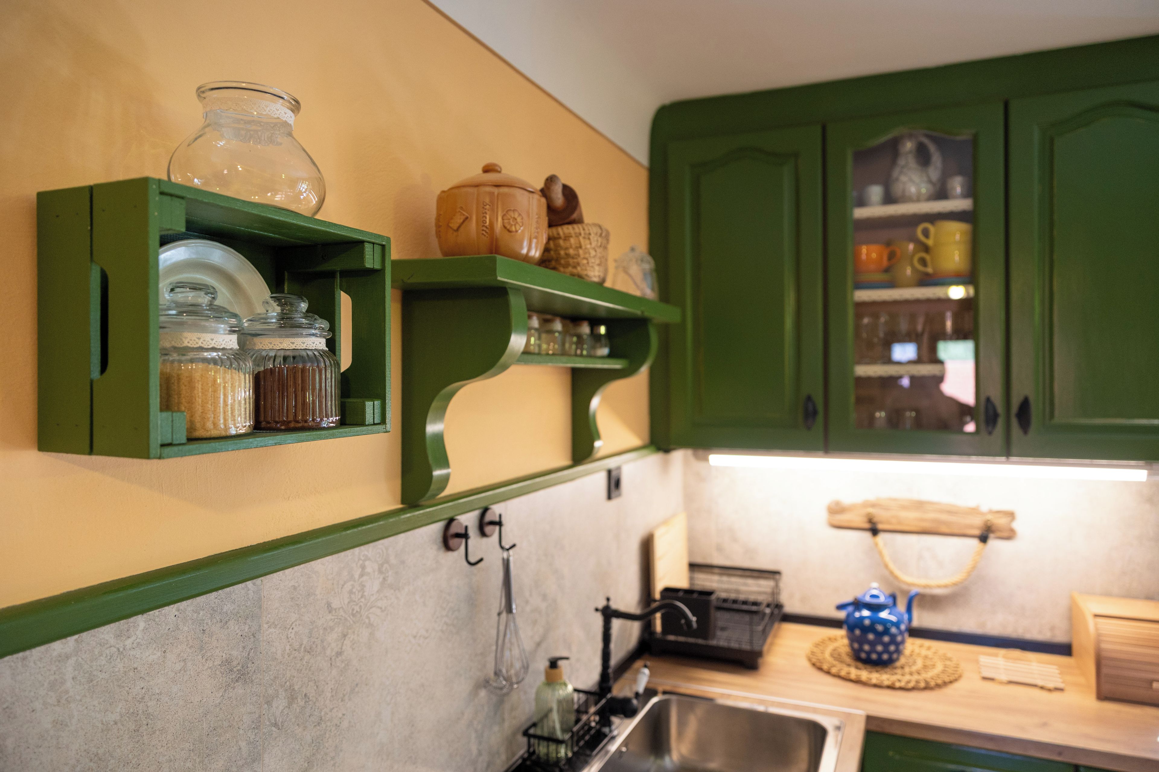 A kitchen with green cabinets, a sink, and various kitchen items on open shelves.