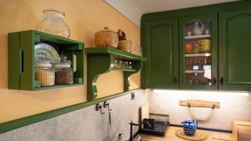 A kitchen with green cabinets, a sink, and various kitchen items on open shelves.