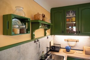 A kitchen with green cabinets, a sink, and various kitchen items on open shelves.