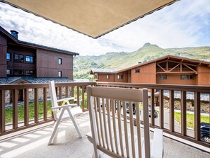 A balcony with a view of a mountain, wooden buildings, and a white chair. - Cozy apartment - 4 guests (Les Menuires)