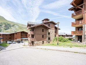 A multi-story hotel with balconies, a stone facade, and a mountainous backdrop. - Cozy apartment - 4 guests (Les Menuires)