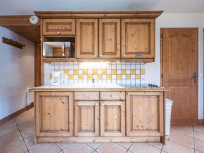 A kitchen with wooden cabinets, a tiled backsplash, and a white sink. - Cozy apartment - 4 guests (Les Menuires)