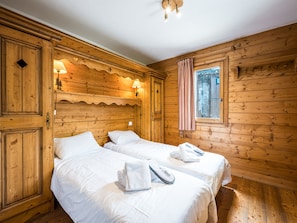 A wooden cabin room with two beds, a window with curtains, and a lamp. - Cozy apartment - 4 guests (Les Menuires)