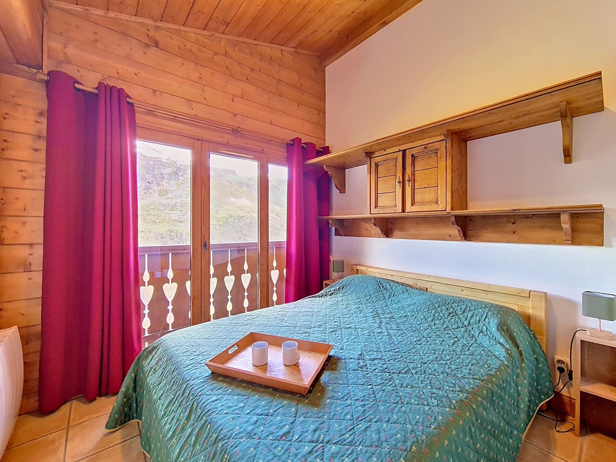 Una habitación de cabaña de madera con una cama, una ventana con cortinas y una repisa sobre la cama.