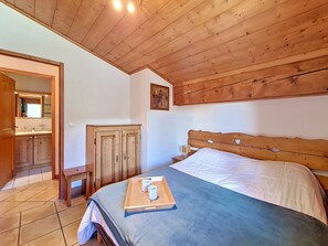 Ein Schlafzimmer mit Holzboden, einem Bett mit blauer Bettdecke, einem Nachttisch aus Holz mit Lampe und einem Holzschrank.