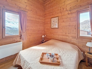 A cozy wooden room with a bed, a tray with cups and a pot, and a window with a view of a snowy landscape. - Bright apartment with balcony - 4 guests (Les Menuires)