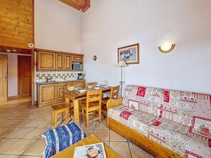 A cozy living room with a wooden sofa, a dining table with chairs, and a kitchen area with wooden cabinets and a microwave. - Bright apartment with balcony - 4 guests (Les Menuires)