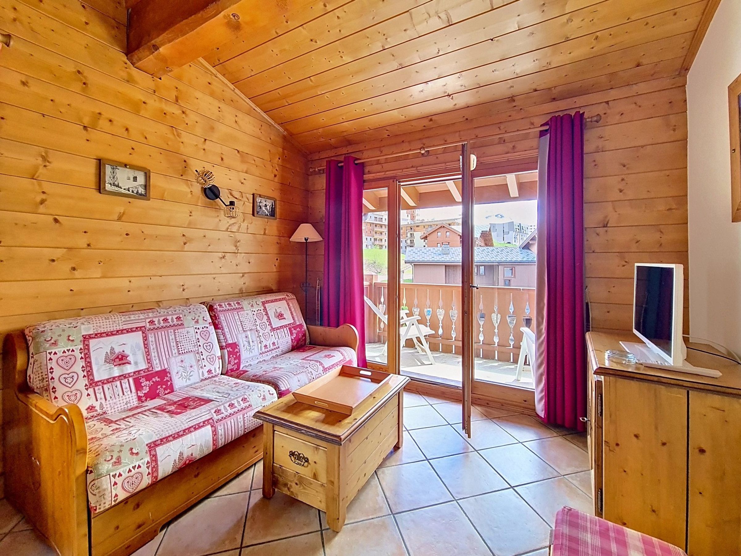 Interno di una baita in legno con divano, un tavolino, televisione e un balcone vista esterna.