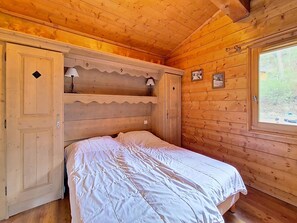 A wooden cabin room with a bed, a shelf, and a window. - Spacious apartment near slopes - 6 guests (Les Menuires)