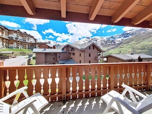 A balcony with a view of a mountain landscape, wooden buildings, and a clear sky. - Spacious apartment near slopes - 6 guests (Les Menuires)