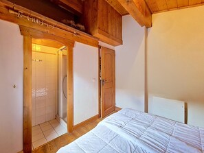 A bedroom with a wooden ceiling, a bed with white bedding, a wooden wardrobe, and a shower area. - Spacious apartment near slopes - 6 guests (Les Menuires)