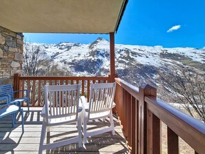 Eine Holzterrasse mit weißen Stühlen mit Blick auf ein schneebedecktes Gebirge.