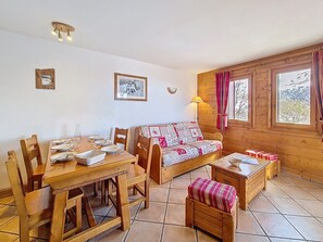 Ein gemütliches Zimmer mit einem Holztisch, der zum Essen gedeckt ist, einer Couch mit gemustertem Bezug und einem Fenster mit Vorhängen.