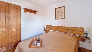 A bedroom with a wooden bed, a wooden wardrobe, a bedside table with a lamp, and a tray with cups and a pot on the bed. - Spacious apartment with terrace - 4 guests (Les Menuires)
